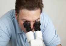 Ein Mann im Hemd schaut durch ein Mikroskop - nur so sind Milben für Menschen sichtbar.